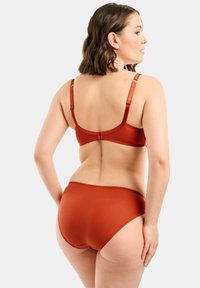 Red seamless bra and brief set made of smooth fabric. Adjustable straps, classic cut with subtle trimming along the edges and no noticeable patterns.