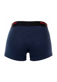 Navy blue boxer shorts with a black elastic waistband featuring red "HUGO" branding. Smooth texture and fitted design.