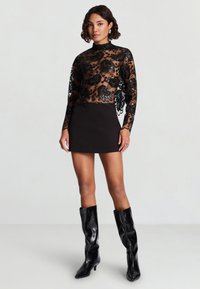 Top in pizzo nero con ricamo floreale, collo alto e maniche lunghe, abbinato a una minigonna nera aderente e stivali neri al ginocchio.