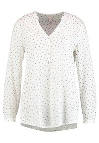 Blusa a maniche lunghe con bottoni in tessuto crema con scollatura a V. Presenta un motivo geometrico blu e rosso. Orlo dritto con spacchi laterali.
