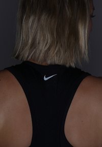 Czarny sportowy top bez rękawów z teksturowanej powierzchni, z małym białym logo Nike blisko dekoltu i wycięciem na plecach.