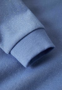 Tela de sudadera azul con una textura fina y brillante. Puños acanalados y superficie suave, que resaltan un diseño cómodo y acogedor.