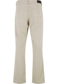 Jeans acampanados beige hechos de una mezcla de algodón, con dos bolsillos traseros y una etiqueta negra en la cintura con detalles de costura.