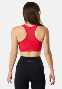 Punainen urheiluliivi, jossa on urheilullinen takatuki ja verkkoyksityiskohtia, yhdistettynä korkeavyötäröisiin mustiin leggings-housuihin, joissa on logo.