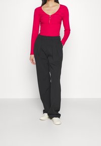 Top aderente fucsia a maniche lunghe con scollatura a V e zip argentata. Pantaloni neri a vita alta plissettati e sneakers bianche completano il look.