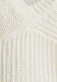 Gruby sweter w kolorze off-white z dekoltem w kształcie litery V, z prążkowanymi wzorami i teksturowanymi ściegami, które dodają wizualnej głębi i ciepła.