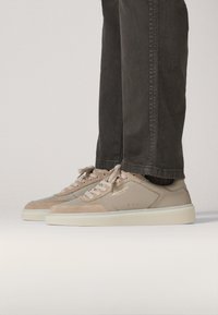 Zapatillas deportivas beige hechas de cuero y ante, con cordones redondos, una suela crema y un sutil logo en el lateral.