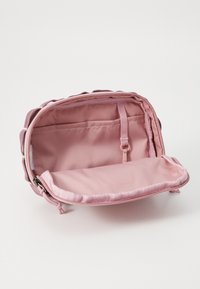 Vaaleanpunainen vetoketjullinen laukku, jossa on pehmeä kangasvuori, sisätasku ja tasainen pohja vakauden takaamiseksi, kun laukku asetetaan alas.