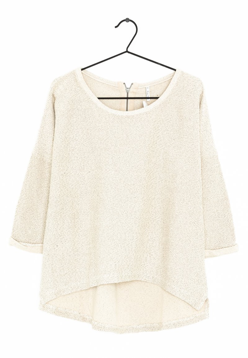 Jasnobeżowa bluzka z długim rękawem o teksturowanym wykończeniu, okrągłym dekolcie i lekko zaokrąglonym dolnym wykończeniem. Posiada zamek z tyłu.