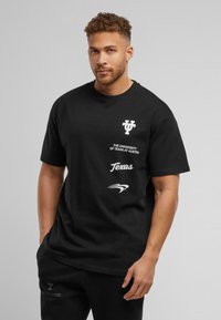 Must must t-särk, millel on "Texase ülikool Austinis" logo ja valged graafikud. Lühikesed varrukad, mugav lõige ja ümar kaelus.