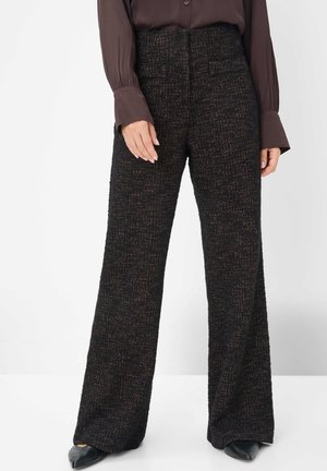 Pantaloni a gamba larga in tessuto nero testurizzato con un sottile motivo, dotati di tasche frontali e design a vita alta. Scarpe nere lisce.