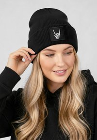 Black knit beanie featuring a square patch with a white skeleton hand graphic. Ribbed texture, snug fit, and top seam.