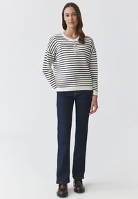 Striped sweater in cream and navy with three-button placket, relaxed fit, and ribbed cuffs, paired with dark blue jeans and brown shoes.