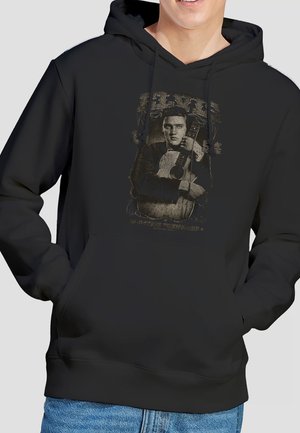 Person wearing a black hoodie with a vintage-style graphic of a man holding an acoustic guitar on the front.