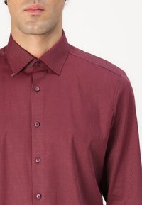 Chemise bordeaux à manches longues avec un motif texturé, dotée d'un col pointu et de boutons assortis, mettant en avant un design ajusté.