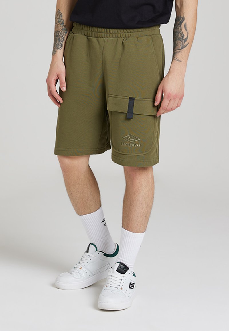 Shorts cargo de culoare verde olive, cu talie elastică, buzunar lateral și logo embosat. Purtați cu pantofi sport albi și șosete albe cu model.