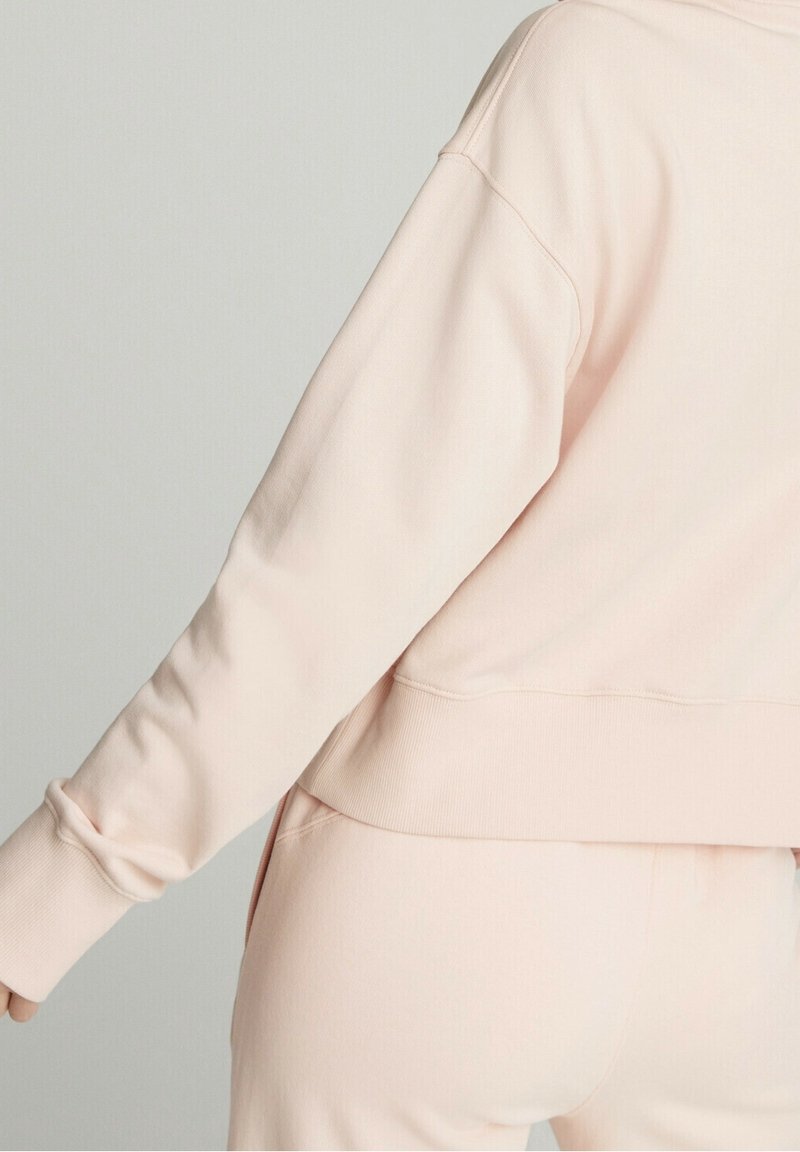 Felpa rosa chiaro con vestibilità comoda, polsini e orlo a coste, realizzata in materiale morbido. Dettagli cuciture visibili sul retro.