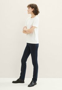 T-shirt blanche à manches courtes associée à un jean slim bleu foncé et des chaussures noires. La t-shirt a une coupe décontractée ; le jean présente des coutures contrastantes.
