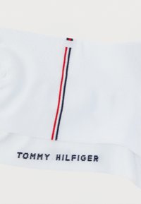 Λευκή βαμβακερή κάλτσα με κόκκινες και μπλε ναυτικές ρίγες. Το "TOMMY HILFIGER" είναι κεντημένο με μαύρα γράμματα κατά μήκος της γάμπας. Ομαλή υφή.