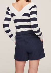 Gestreiftes Langarmshirt in Weiß und Marineblau mit V-Ausschnitt auf der Rückseite; kombiniert mit strukturierten Marineblau-Shorts mit Taschen und elastischem Bund.