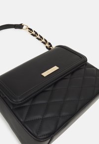 Sac à main noir matelassé avec un accent en métal doré et une anse en chaîne tressée. Texture lisse avec une fermeture à rabat.