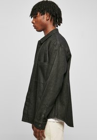 Camicia in denim nero con design colletto, polsini a bottone, tasca anteriore e vestibilità ampia. Presenta un tessuto testurizzato e una silhouette pulita e semplice.