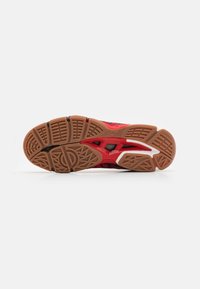 Suela de zapatilla deportiva en rojo y negro con goma texturizada, que presenta un patrón de piso único y cortes en la entresuela para tracción y soporte.
