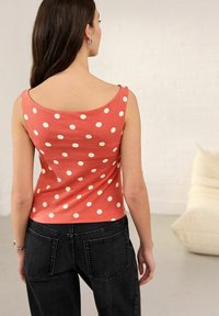Débardeur corail à pois blancs, avec un décolleté large et une coupe ajustée. Associé à un jean noir taille haute.
