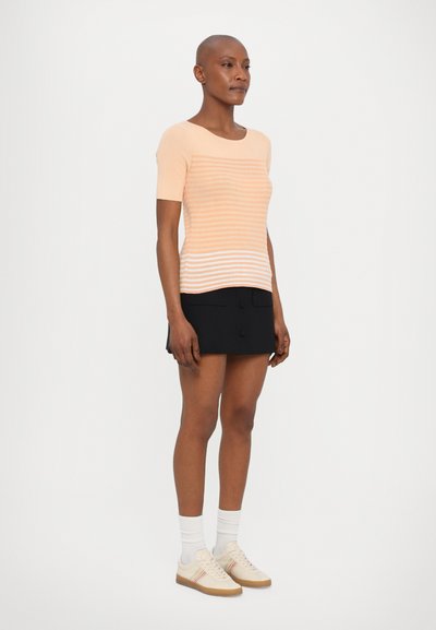 Perzik gestreepte gebreide top met korte mouwen, gecombineerd met een zwarte minirok. Beige sneakers met subtiele kleuraccenten en witte sokken.