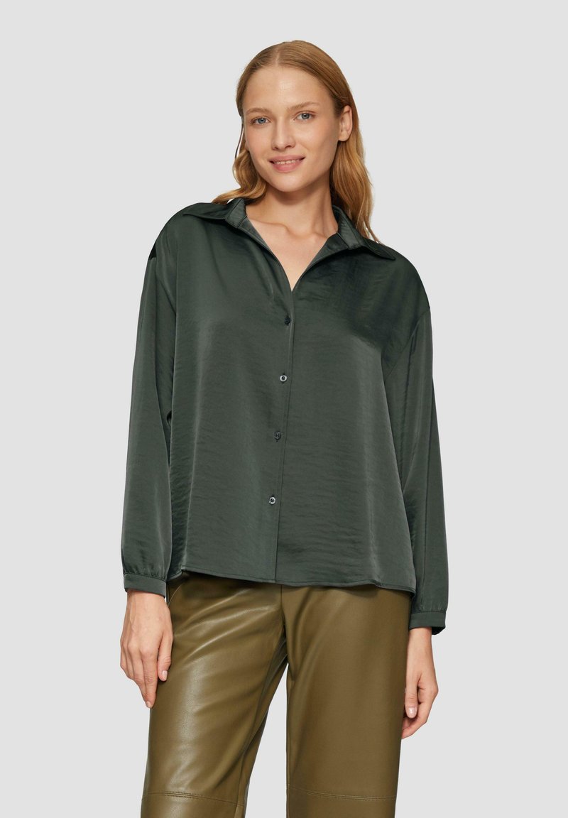 Chemise boutonnée vert foncé en tissu lisse, avec un col, des manches longues et une coupe décontractée, associée à un pantalon en cuir vert olive.