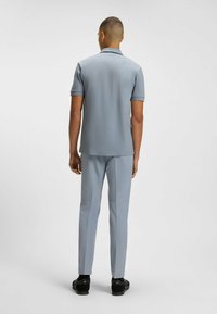 Jasnoszara polo z krótkim rękawem, widok z tyłu. Połączona z dopasowanymi spodniami i czarnym obuwiem. Gładka tekstura, nowoczesny krój.