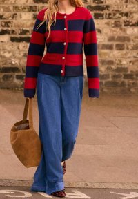 Cardigan a rayas rojas y marinas con botones y bolsillos, combinado con jeans de pierna ancha azules y un bolso de ante marrón. Material de punto texturizado.