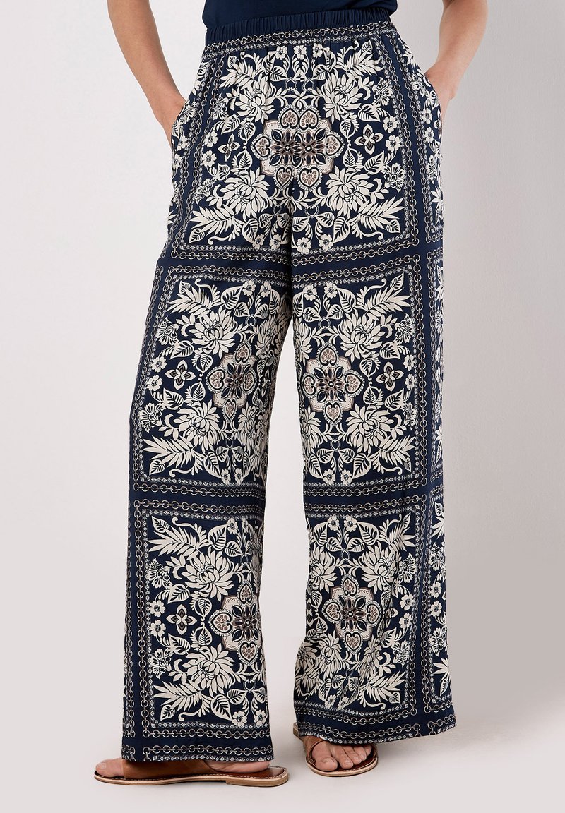 Marineblaues florales Muster bei weiten Hosen mit Kordelzugbund, die große weiße Blumenmuster und seitliche Taschen aufweisen. Glatte Stofftextur.