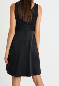 Czarna sukienka bez rękawów z dopasowaną górą, koronkowym wykończeniem i rozkloszowanym dołem. Gładka tekstura i długość do kolan. Zamek błyskawiczny z tyłu widoczny.