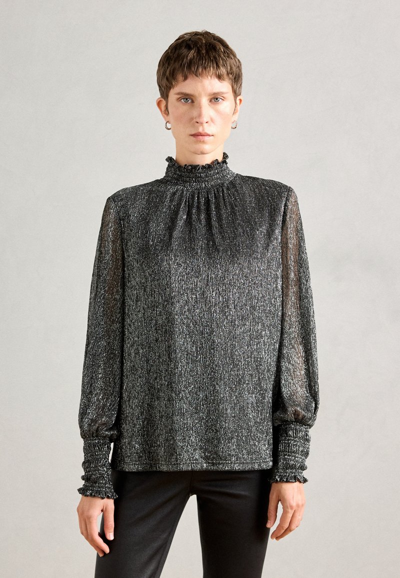 Blusa nera a maniche lunghe con colletto alto a volant e polsini elasticizzati. Il tessuto ha una texture scintillante con accenti argentati.