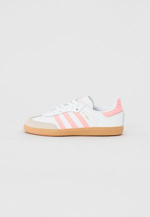 Baskets basses Adidas Samba blanches et roses avec semelle en gomme et bout en daim présentées sur un fond gris clair uni.
