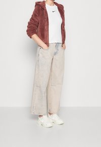 Burgundowy polarowy hoodie na zamek z kapturem, w połączeniu z białą koszulką Nike z krótkim rękawem i jasnoniebieskimi dżinsami w szerokim kroju. Białe sneakersy.