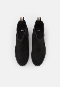 Černé semišové kotníkové boty s hladkým povrchem, vybavené kontrastním pruhovaným poutkem a logem uvnitř. Elegantní, minimalistický design.