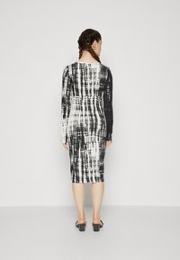 Long-sleeve, fitted dress in black and white tie-dye pattern, knee-length with a round neckline, textured fabric, and a bodycon silhouette.