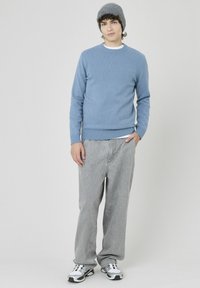 Pull en tricot bleu clair avec des poignets et un ourlet côtelés, associé à un jean gris baggy et des baskets blanches. Le modèle porte un bonnet en tricot gris.