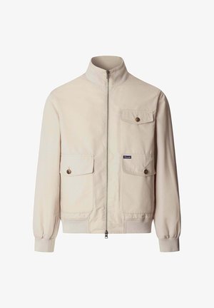 Chaqueta beige claro con cremallera, cuello alto, dos grandes bolsillos con solapa y botones en la cintura, y un bolsillo con solapa en el pecho.