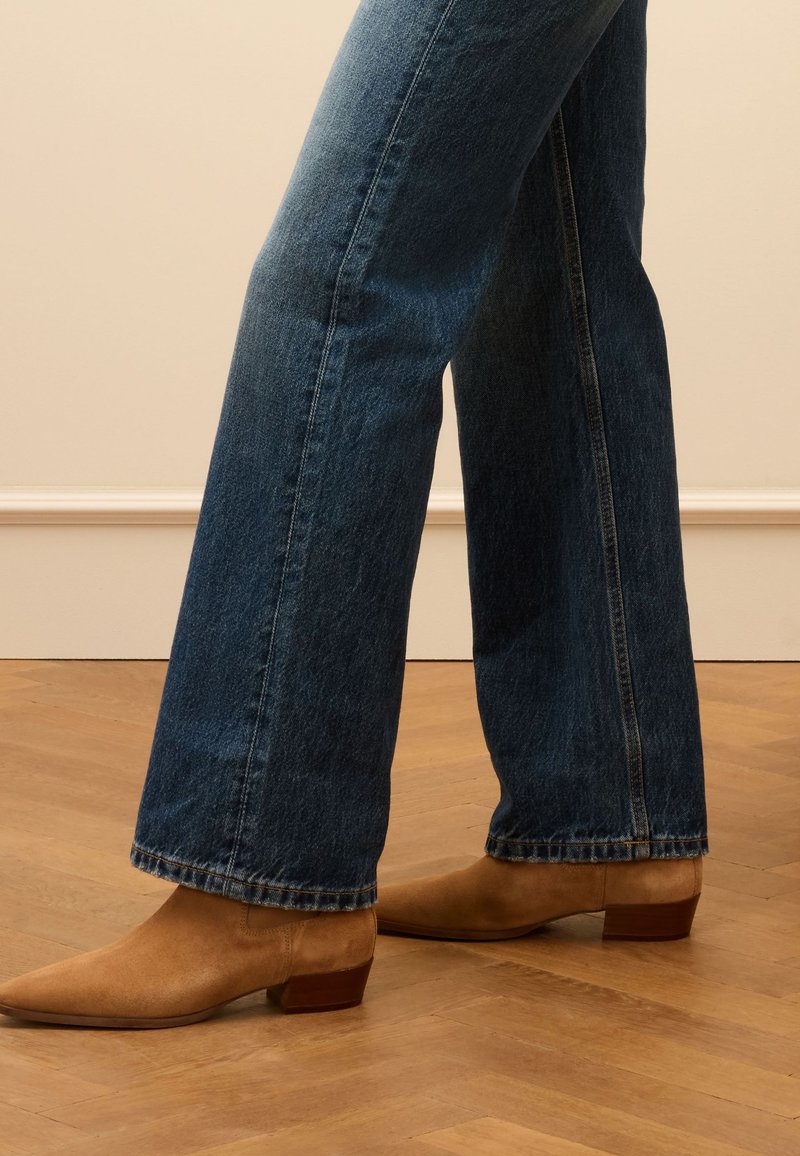 Jeans flare en denim bleu avec des ourlets effilochés, assortis à des bottines à bout pointu en daim beige avec un petit talon bloc.