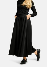 Melna gara svārki no plūstoša materiāla ar augstu jostasvietu un sānu kabatām, apavi melni loaferi. Virsdrēbe ar tekstūru un mirdzumiem.