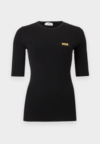 T-shirt noir côtelé à manches courtes avec un col rond et une poche poitrine gauche ornée d'un détail doré. Texture douce sur toute la surface.