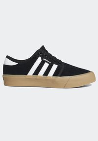 Svarta mockaskor med vita ränder, gummisulor i beige, rund tå och vanlig snörning. Har varumärkeslogotyp på sidan.