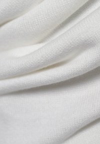 Weißer strukturierten Stoff mit sichtbarem Strickmuster, der eine weiche, glatte Textur und leicht variierende Dicke in Wellen zeigt.