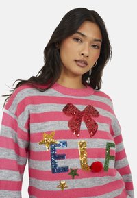 Pull rayé rose et gris avec un nœud en sequins rouges et des lettres en sequins colorés "E.L.F.", rehaussé d'étoiles et d'un détail en pompon.
