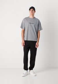 Grå bomulds T-shirt med rund halsudskæring og korte ærmer, der har "Calvin Klein" logo. Kombineret med sorte bukser og hvide sneakers.
