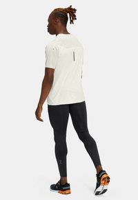 Lys grå kortærmet skjorte med en ryggående sømdetalje, sorte leggings og sorte løbesko med orange accenter.
