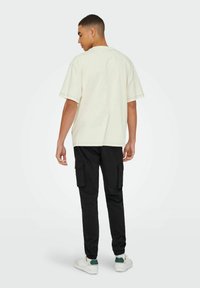 Lys beige oversized t-shirt med korte ærmer, parret med sorte cargo-bukser med sidelommer og elastiske manchetter, båret med hvide sneakers.
